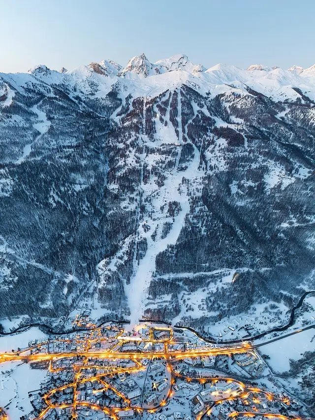 Aerial view of a Serre Chevalier village at dusk, its streets lit below the snowy ski slopes