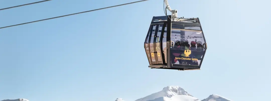 A Serre Chevalier Vallée gondola against a blue sky above snowy peaks