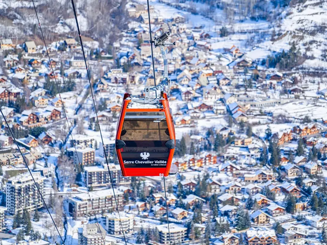 A red Serre Chevalier gondola above the snow-covered rooftops of Briançon